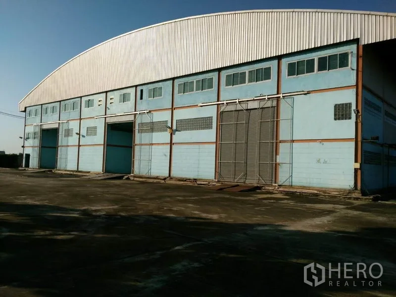 Factory for sale in Lat Lum Kaeo, Pathum Thani - Wide concrete yard facing a high-clearance warehouse with multiple large loading bays and sliding doors.