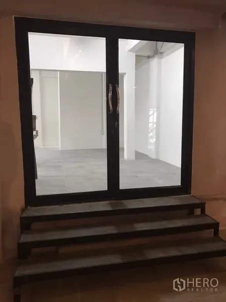 办公空间 出租在Watthana, Bangkok - 黑色框架的双扇玻璃门与台阶入口，通向明亮的办公区。