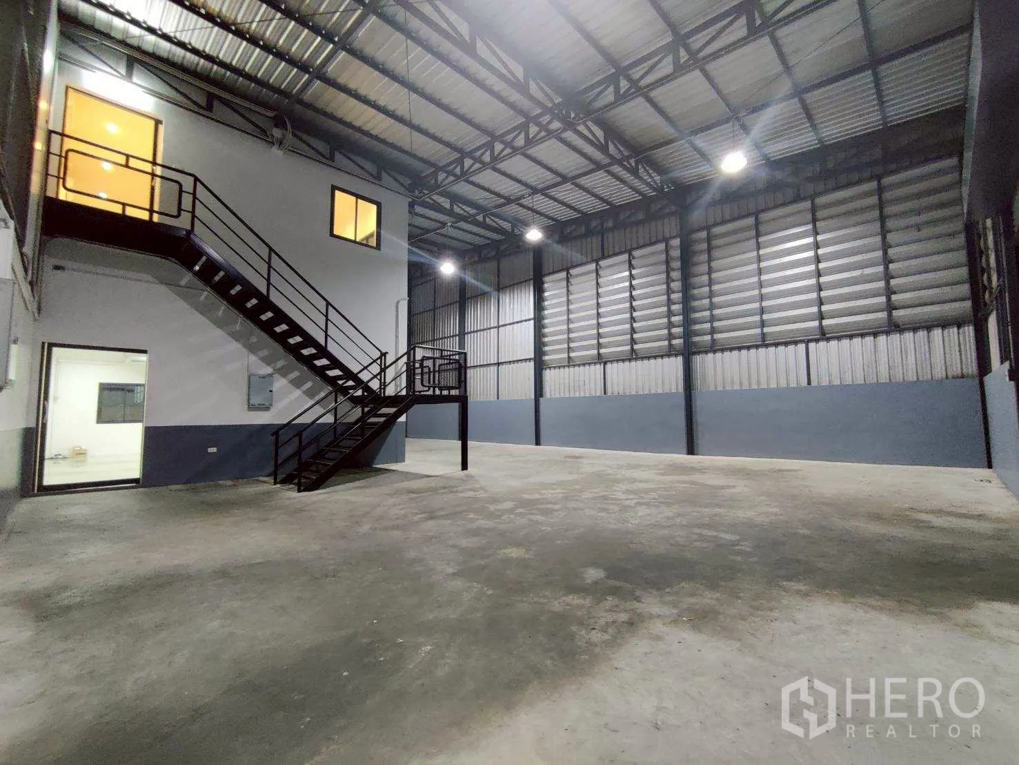 Warehouse for rent in Lam Luk Ka, Pathum Thani - Overview of the high-roof warehouse with mezzanine rooms and bright lighting.