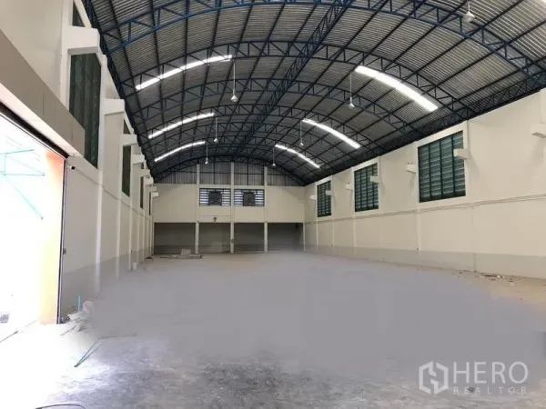 工厂 出租在Samut Prakan - 高挑拱形钢结构屋顶的宽敞仓库内部，照明充足，尽头带有夹层办公室。