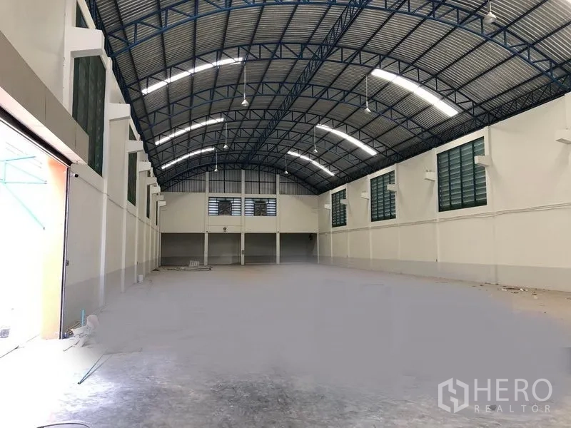 工厂 出租在Samut Prakan - 高挑拱形钢结构屋顶的宽敞仓库内部，照明充足，尽头带有夹层办公室。