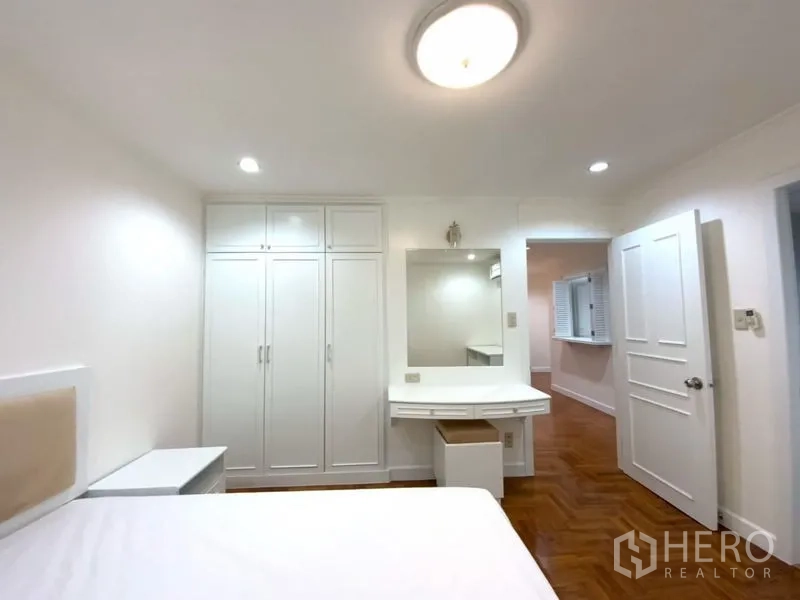 公寓 出租在Watthana, Bangkok - 卧室配白色壁柜与梳妆台，木地板与简洁白墙。