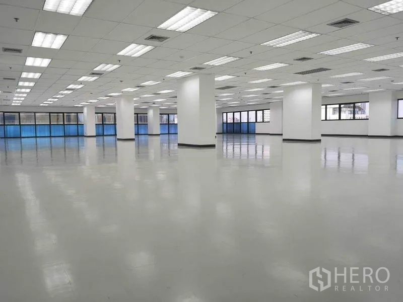 Office Space for rent in Phaya Thai, Bangkok - Unfurnished office hall with evenly spaced columns, drop ceiling lights and blue sunshades along the windows.