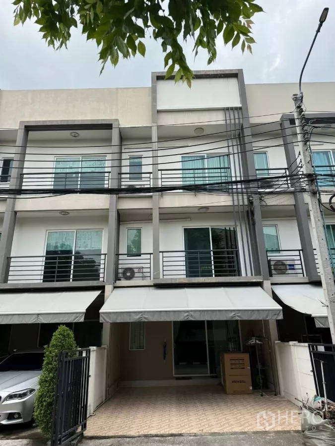 Townhouse for rent in Suan Luang, Bangkok - Modern 3-storey townhouse facade with gated parking and awnings in Suan Luang, Bangkok.