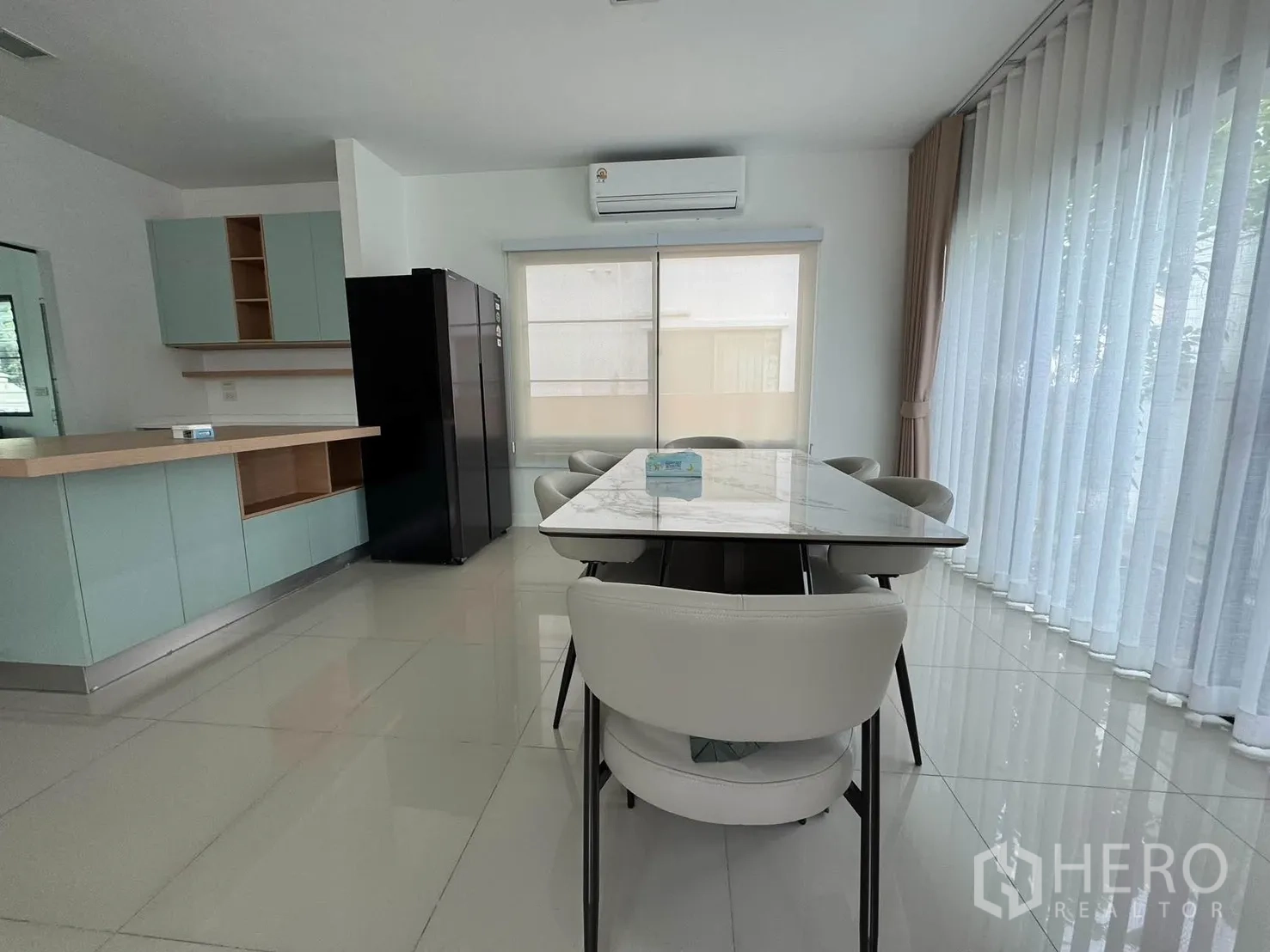 Detached House for rent in Prawet, Bangkok - Open-plan dining space with sheer curtains, built-in pastel kitchen cabinets, and a black refrigerator.