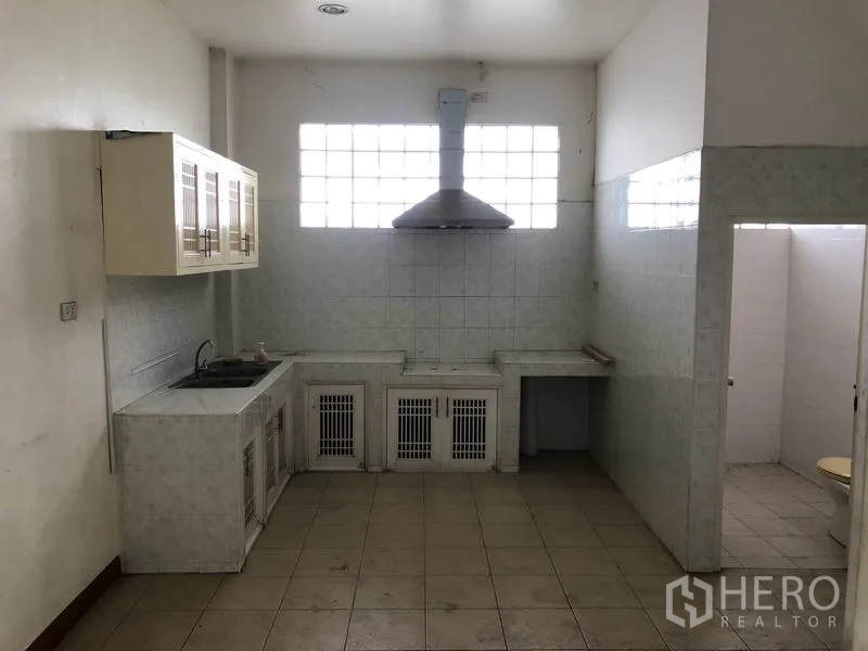 Factory for rent in Sai Noi, Nonthaburi - Staff pantry with tiled counters, sink, cooker hood and an adjacent restroom.