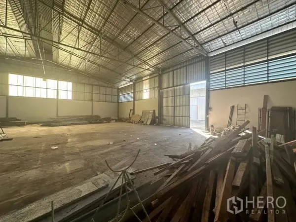 คลังสินค้า ให้เช่าในSaphan Sung, Bangkok - พื้นที่โกดังกว้างเห็นประตูเหล็กบานสไลด์ ช่องลมระบายอากาศ และไม้กองอยู่มุมห้อง
