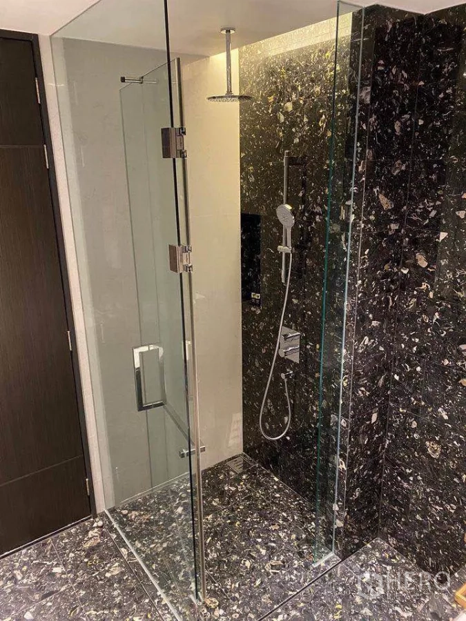 Condominium for rent or sale in Khlong Toei, Bangkok - Bathroom with glass‑enclosed rain shower and dark stone feature walls.