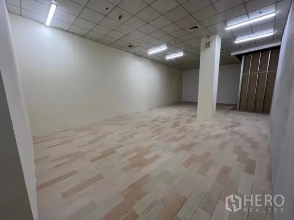 Retail Space for rent in Watthana, Bangkok - Open-plan retail interior with light wood-look tiles, grid ceiling, central support column and bright strip lighting.