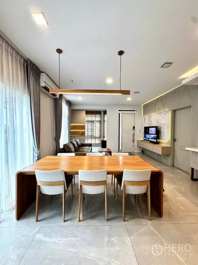 Detached House for rent in Prawet, Bangkok - Dining area with wooden table, six chairs and pendant lighting next to large windows.