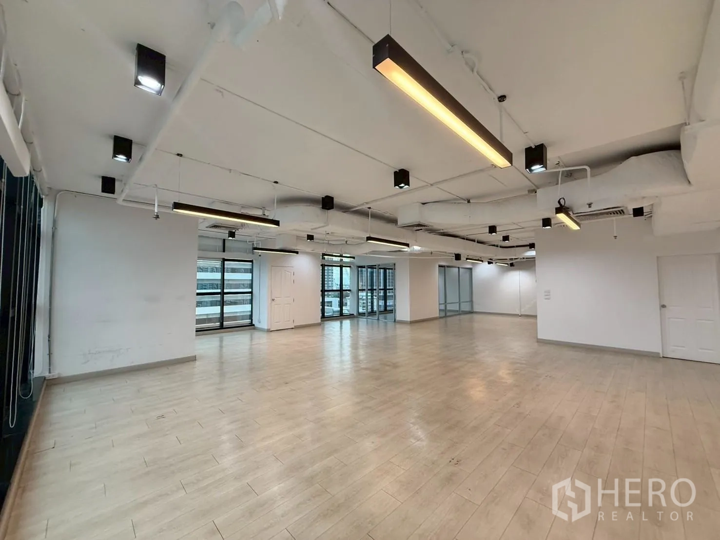 Office Space for rent in Watthana, Bangkok - Wide office floor with suspended lights, glass partitions, and a white door.