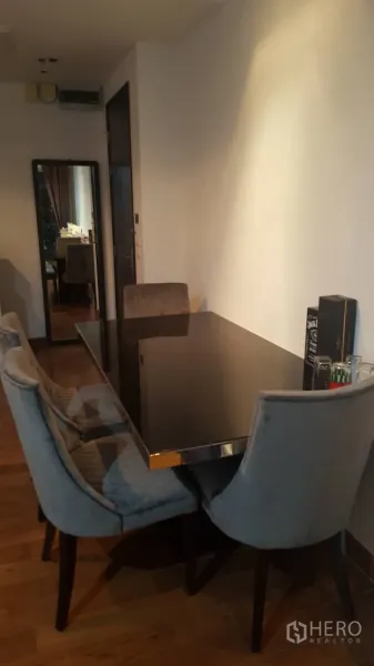 Condominium for rent in Pathum Wan, Bangkok - Cozy dining corner with a black glass table, four upholstered chairs and warm wood flooring in a modern Bangkok condo.