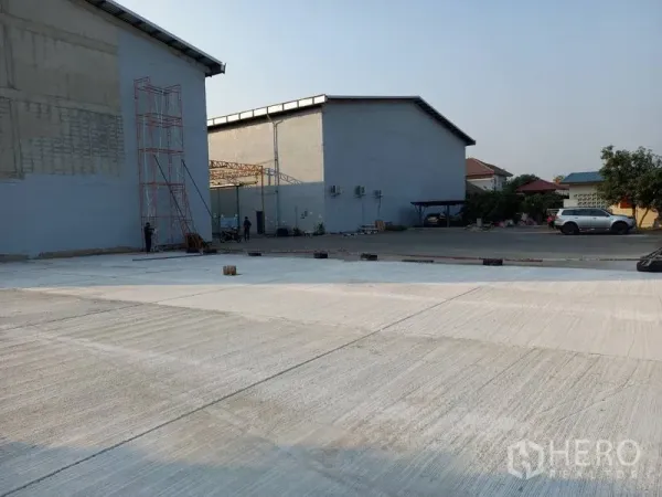 Warehouse for rent in Mueang Pathum Thani, Pathum Thani - Open concrete yard beside warehouse blocks suitable for truck maneuvering and parking.