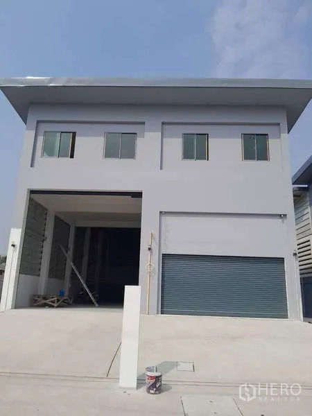 Warehouse for rent or sale in Krathum Baen, Samut Sakhon - Front elevation of a grey warehouse showing twin roller shutters and driveway access.