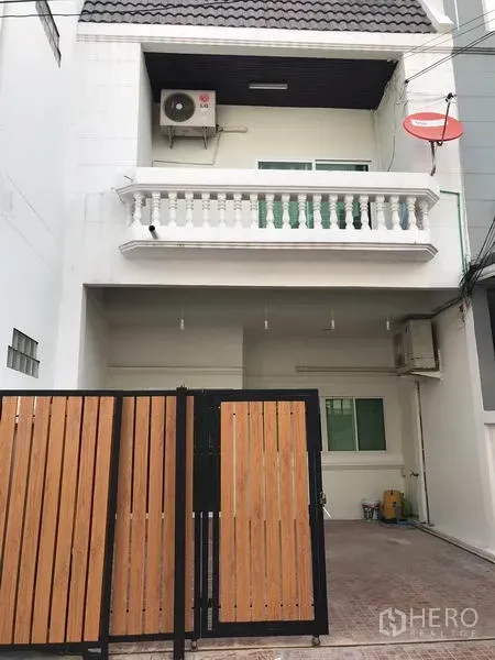 Townhouse for rent or sale in Phra Khanong, Bangkok - White multi-storey townhouse facade with gated carport and balcony.