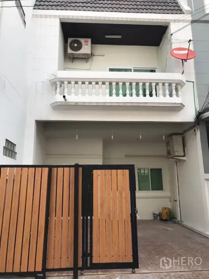 Townhouse for rent or sale in Phra Khanong, Bangkok - White multi-storey townhouse facade with gated carport and balcony.