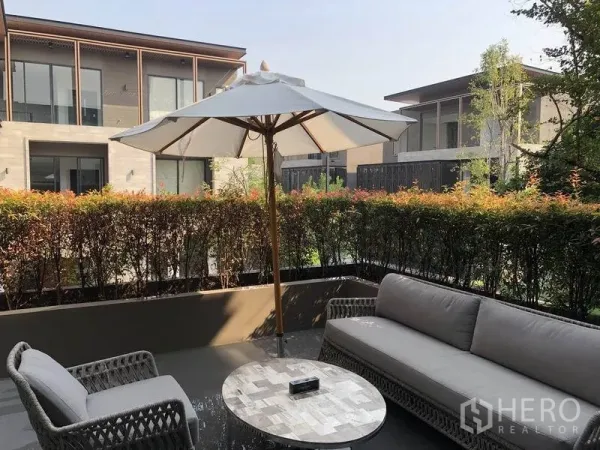 บ้าน ขายในBang Kapi, Bangkok - มุมนั่งเล่นกลางแจ้งพร้อมร่มสนาม เก้าอี้หวาย และพุ่มไม้ตัดแต่ง มองเห็นบ้านสมัยใหม่รอบข้าง.