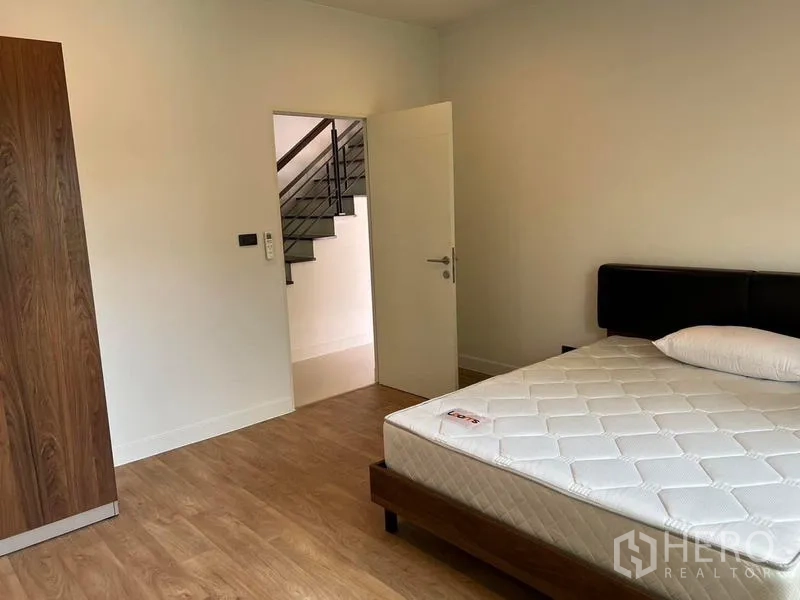 Detached House for rent in Bang Kapi, Bangkok - Bright bedroom with wood flooring, queen bed, wardrobe and doorway to staircase.