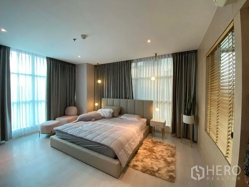 Condominium for sale in Huai Khwang, Bangkok - Spacious master bedroom with king bed, pendant bedside lights, full-height curtains and a corner lounge chair.