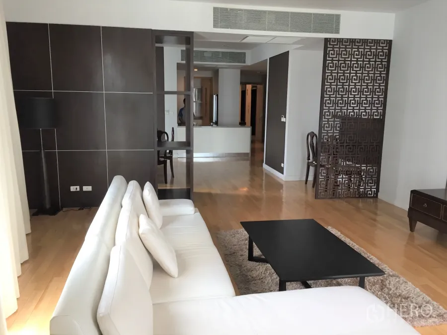 Condominium for rent or sale in Khlong Toei, Bangkok - Spacious living room with white sofa, black coffee table, wood floors and a decorative partition in a modern condo.