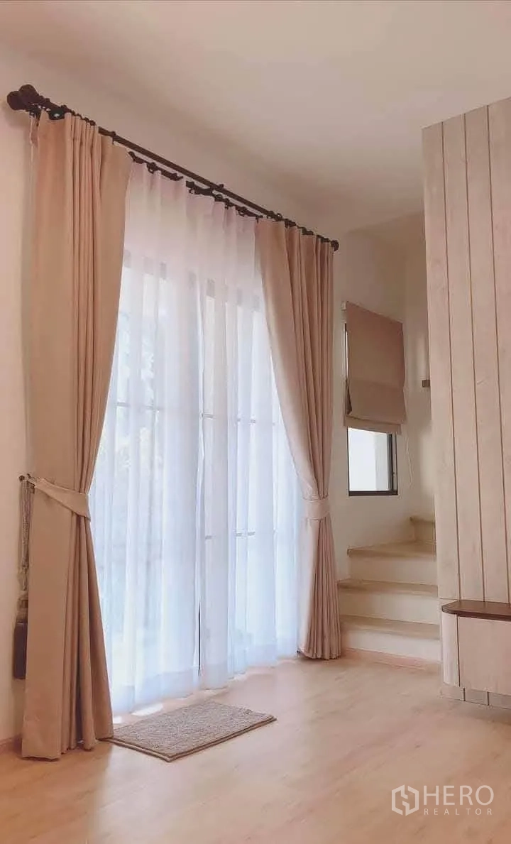 Townhouse for rent in Bang Phli, Samut Prakan - Tall sheer drapes over sliding doors next to a short staircase and feature wall.