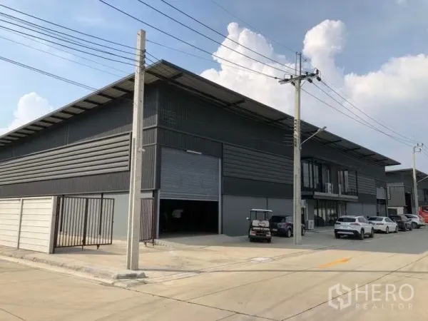 货栈 出租在Bang Phli, Samut Prakan - 邦普里现代灰色仓库外观，配大卷帘门、宽阔混凝土道路和停车位。