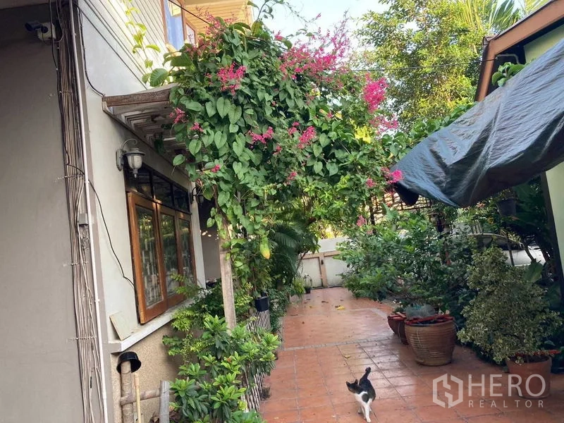 Detached House for sale in Wang Thonglang, Bangkok - Leafy garden walkway with a flowering vine arch and dense greenery along the side of the house.