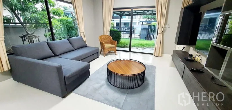 บ้าน ให้เช่าในBang Phli, Samut Prakan - ห้องนั่งเล่นโซฟาสีเทา โต๊ะกลางกลม มองเห็นสวนส่วนตัว