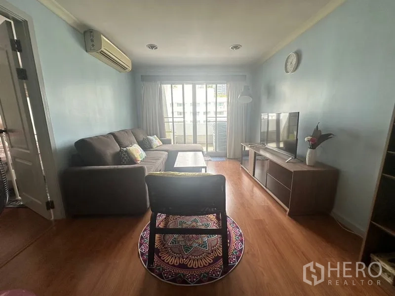 คอนโด ให้เช่าในWatthana, Bangkok - ห้องนั่งเล่นอบอุ่น โซฟาเอล ตู้วางทีวี พื้นไม้ และประตูกระจกสไลด์ออกสู่ระเบียง