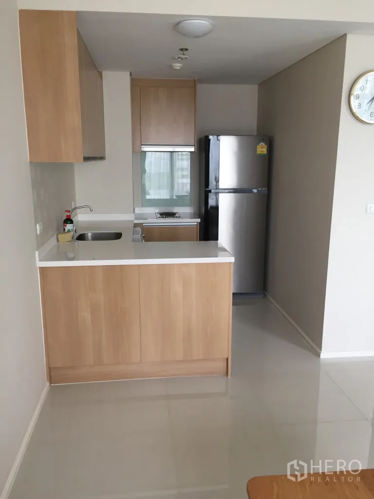公寓 出租在Ratchathewi, Bangkok - 现代小厨房，白色台面、水槽、灶台、冰箱与浅木色橱柜。
