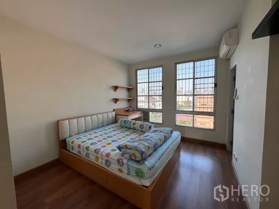 Townhouse for rent in Bang Kho Laem, Bangkok - Sunlit bedroom with large grid windows, wooden floor, air conditioning and corner wall shelves.