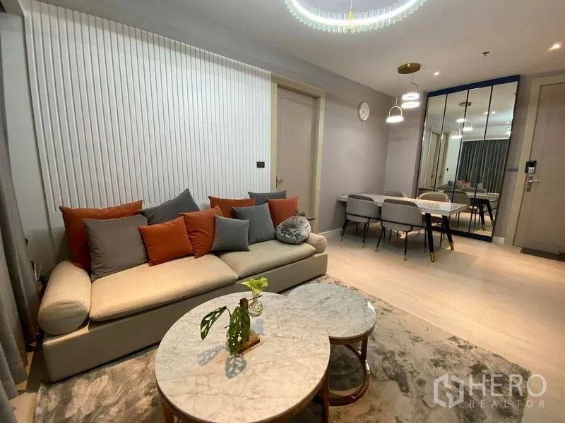 Condominium for sale in Huai Khwang, Bangkok - Open-plan living and dining area with sofa, chandelier, marble tables and a mirrored wall for added depth.