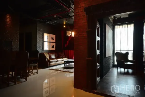 公寓 出租或出售在Khlong Toei, Bangkok - 入口走廊通向客厅，皮沙发、砖墙与落地窗搭配薄纱窗帘。