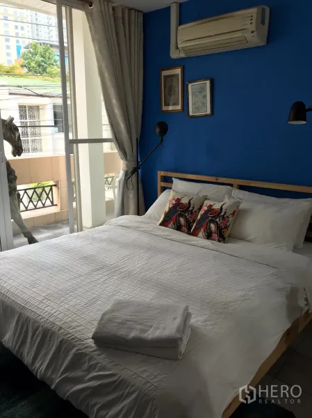 Townhouse for rent in Khlong Toei, Bangkok - Bright bedroom with blue accent wall, large window and air conditioner.