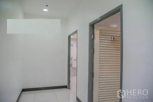 办公空间 出租在Bang Na, Bangkok - 通往洗手间的走廊，白色瓷砖地面与敞开的房门。