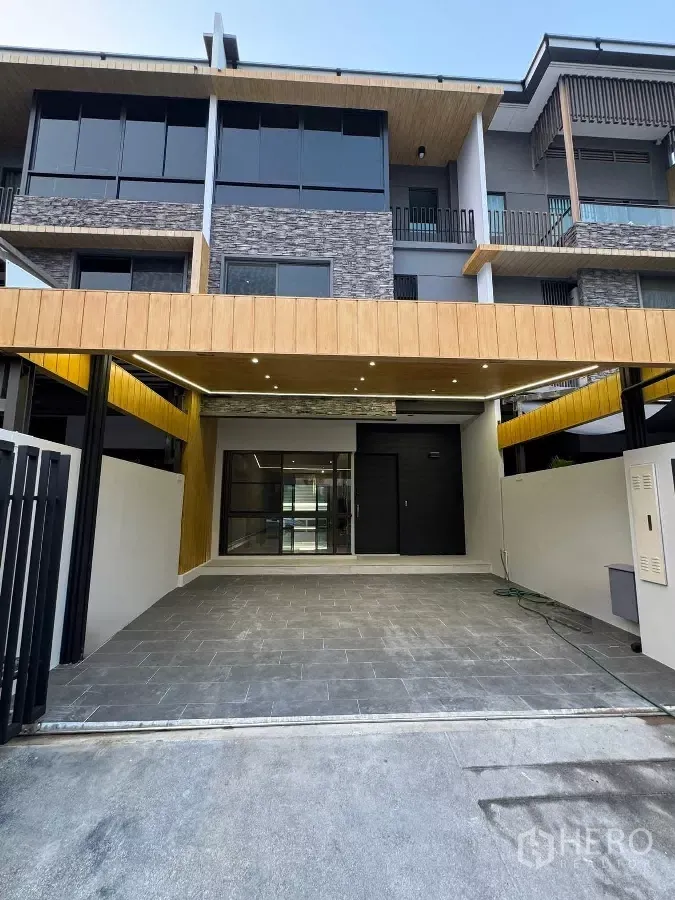 Townhouse for rent or sale in Lat Phrao, Bangkok - Modern three-storey townhouse facade with covered two-car carport and stone accents.