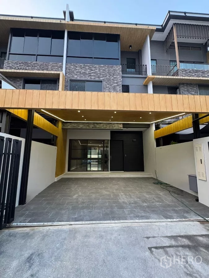 Townhouse for rent or sale in Lat Phrao, Bangkok - Modern three-storey townhouse facade with covered two-car carport and stone accents.