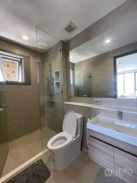 Condominium for rent in Bang Kho Laem, Bangkok - Bright bathroom with glass shower, toilet, and sleek vanity.