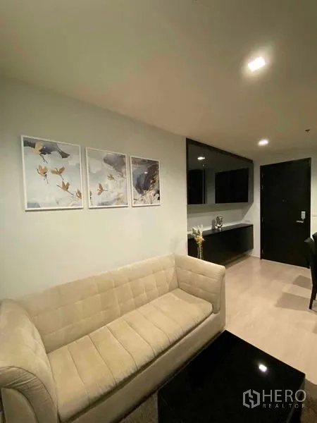 Condominium for rent in Khlong Toei, Bangkok - Living area corridor with beige sofa, wall art and glossy storage cabinets.