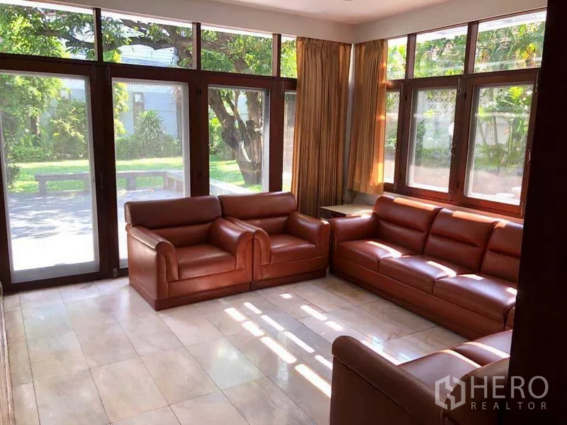 Detached House for rent in Phra Khanong, Bangkok - Sunroom‑style lounge with three leather sofas and floor‑to‑ceiling windows to the garden.
