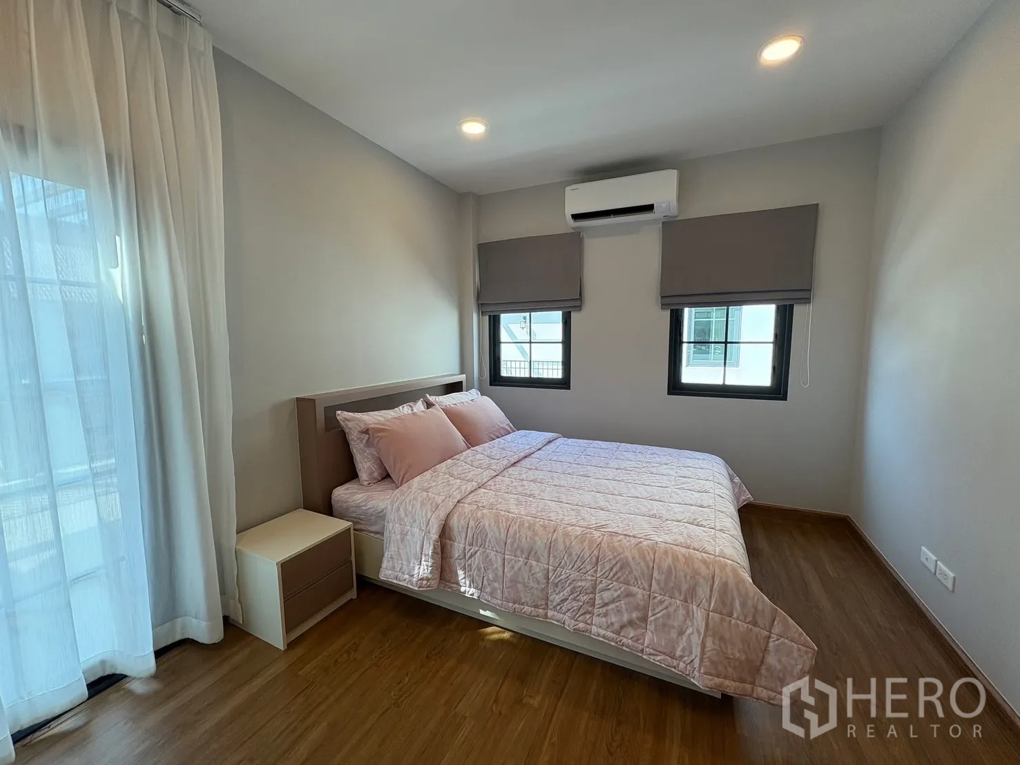 บ้าน for rent in Bang Phli, Samut Prakan - ห้องนอนรับแขกสว่างด้วยชุดเครื่องนอนสีชมพู หน้าต่างสองบาน เครื่องปรับอากาศ และม่านโปร่งบนพื้นไม้.