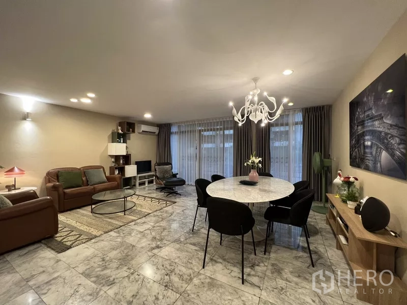 Townhouse for rent or sale in Suan Luang, Bangkok - Open‑plan living and dining room with marble floors, chandelier and full‑height curtains.