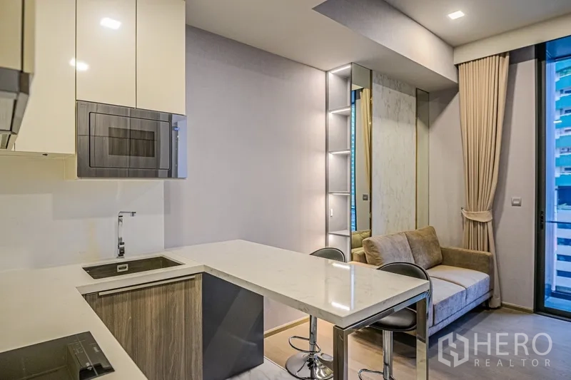 Condominium for rent in Watthana, Bangkok - Compact kitchen with peninsula dining, built-in microwave and a cozy sofa in the open-plan living area.