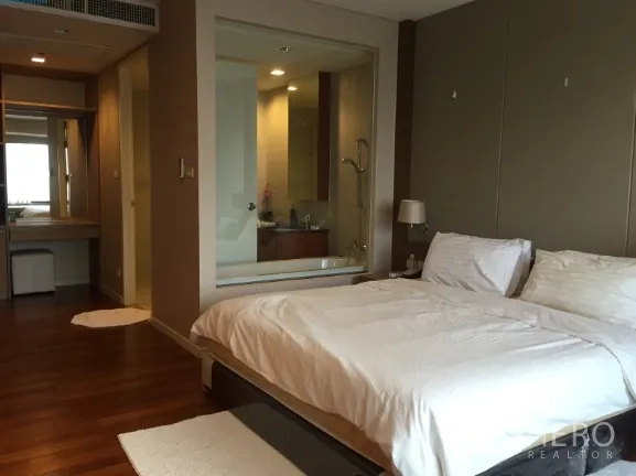 公寓 出租或出售在Sathon, Bangkok - 主卧配白色床品与木地板，玻璃墙浴室设浸泡浴缸与淋浴间。