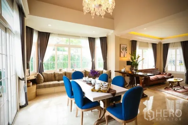 บ้าน ให้เช่าในBang Na, Bangkok - พื้นที่นั่งเล่นและรับประทานอาหารโปร่งสว่าง มีโคมระย้า หน้าต่างบานใหญ่ เก้าอี้ทานข้าวสีน้ำเงิน
