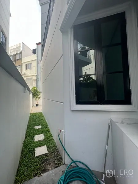 带办公室的家 出租或出售在Watthana, Bangkok - 侧院草坪沿白色外墙铺设踏步石。