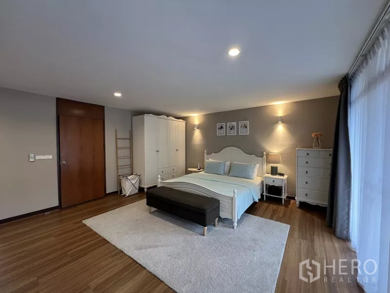 Townhouse for rent or sale in Suan Luang, Bangkok - Generous bedroom with classic white furniture, rug and warm lighting.