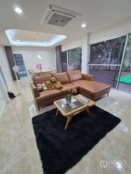 Detached House for rent in Bang Kruai, Nonthaburi - Living room with L-shaped leather sofa, rug and garden views through glass walls.