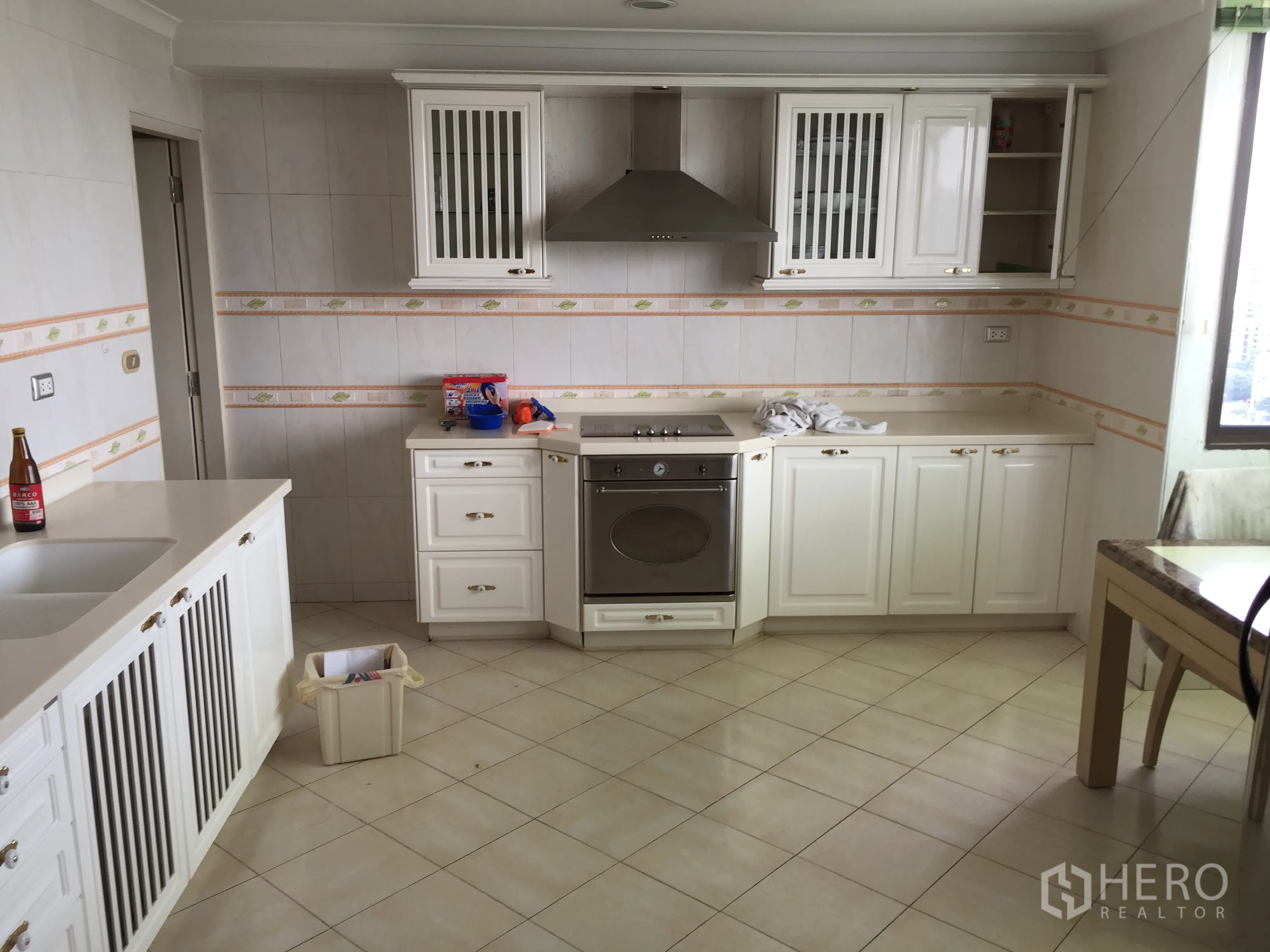 Condominium for rent in Khlong Toei, Bangkok - Bright kitchen with white cabinetry, oven, range hood and tiled floor beside a window.