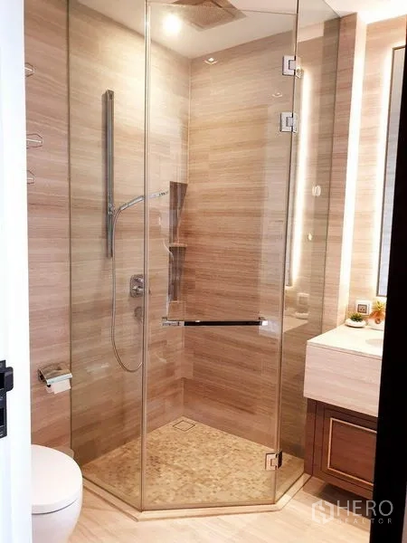 Condominium for rent or sale in Watthana, Bangkok - Modern bathroom featuring a glass-enclosed shower, wall-mounted fixtures and stone tiles.